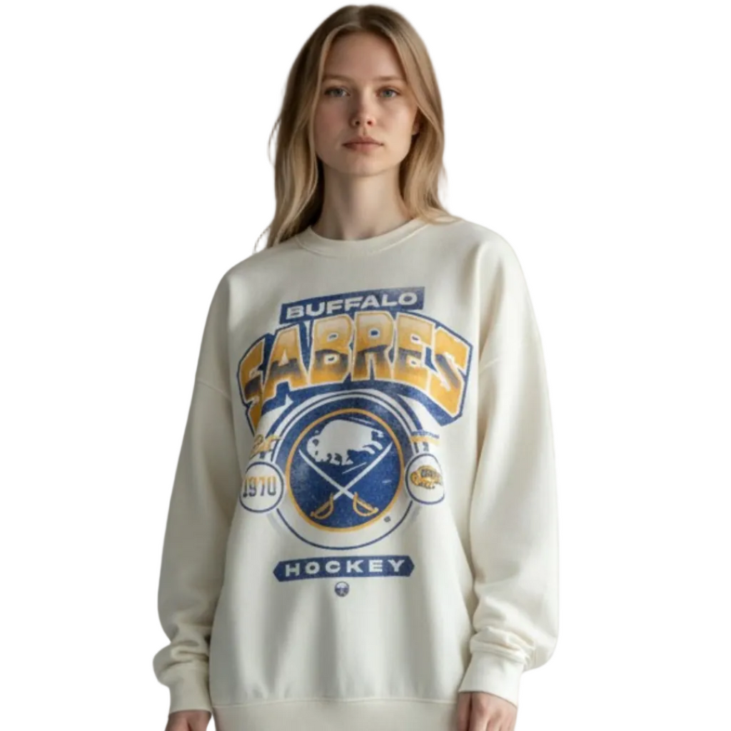 Person wearing a cream-colored sweatshirt with 'Buffalo Sabres' logo on a plain background