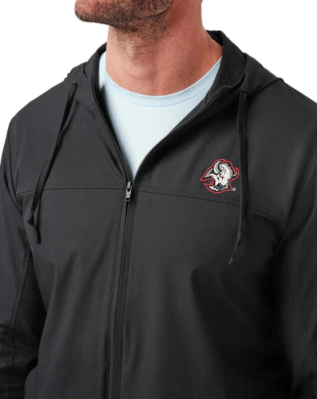 A man wearing a black zip-up hooded jacket with a Buffalo Sabres logo on the left chest, layered over a light blue t-shirt, against a white background.