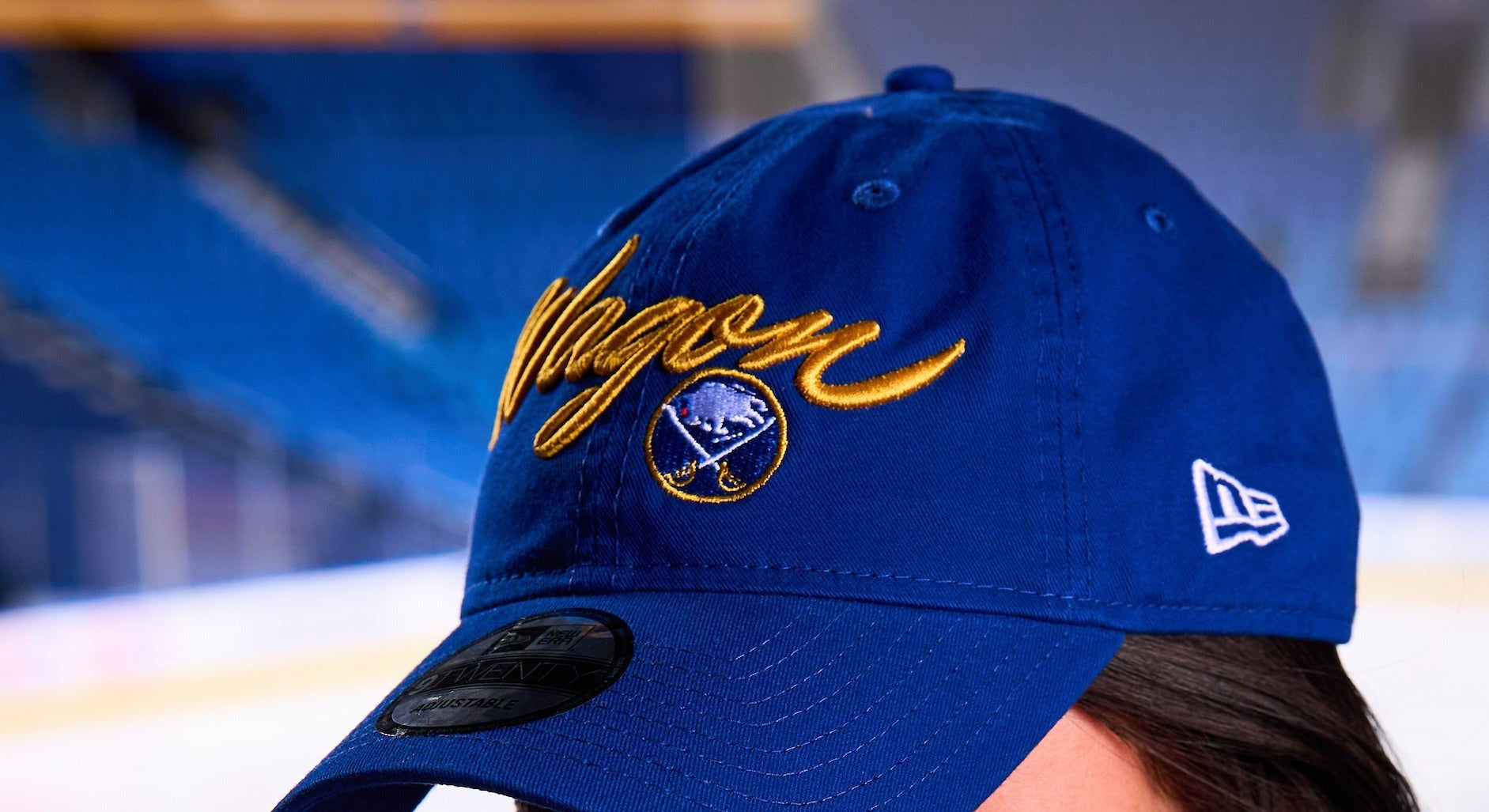 Woman wearing a blue cap with yellow text and a logo in an indoor sports arena.