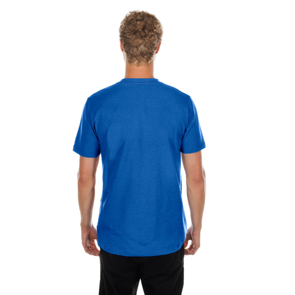 A man viewed from behind wearing a solid royal blue short-sleeve t-shirt and black pants, standing against a plain white background.