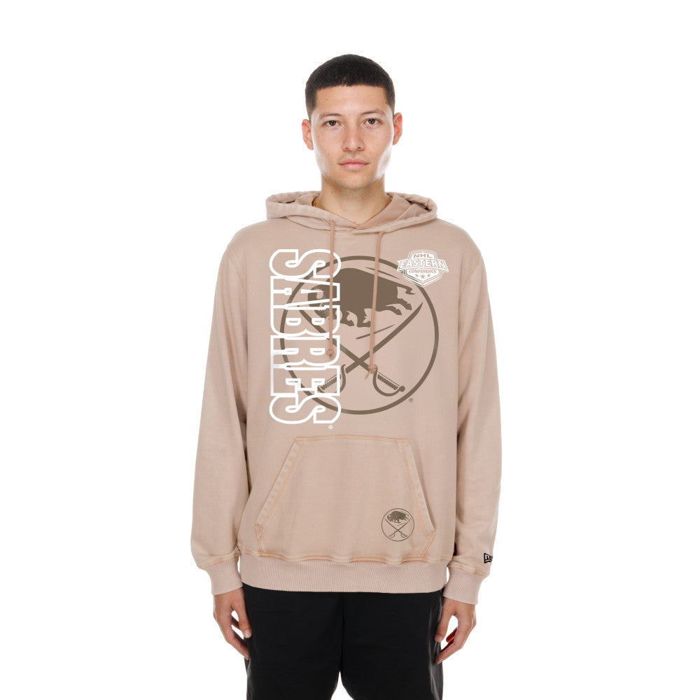 A man wearing a beige Sabres hockey hoodie with a large white and brown graphic on the front, standing against a plain white background.