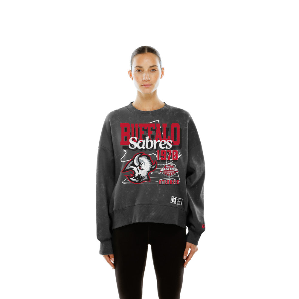 A woman modeling a dark gray washed sweatshirt with a distressed red and white Buffalo Sabres 1978 graphic on the front, paired with black pants against a solid white background.
