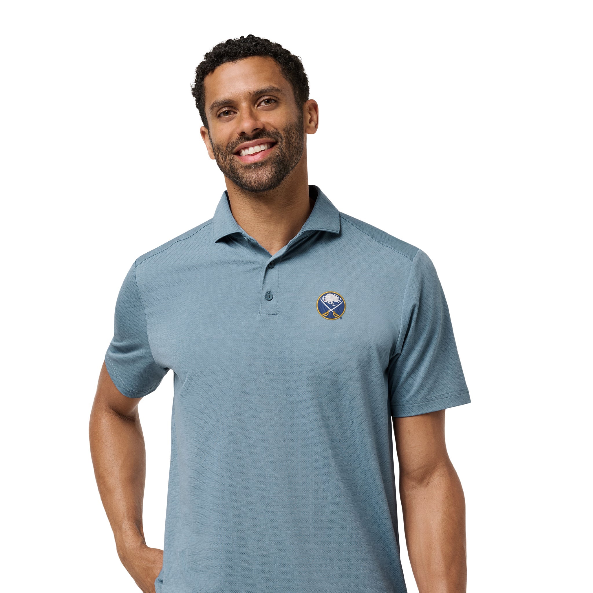 A man wearing a slate blue short-sleeve polo shirt with a small circular embroidered logo on the left chest, paired with black pants, photographed against a plain white background.