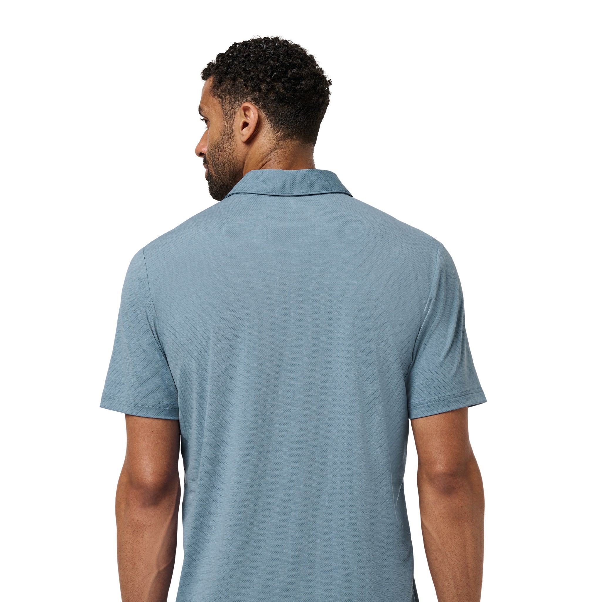 A man viewed from the back wearing a short-sleeve polo shirt in a muted dusty blue color, paired with dark pants, against a plain white background.