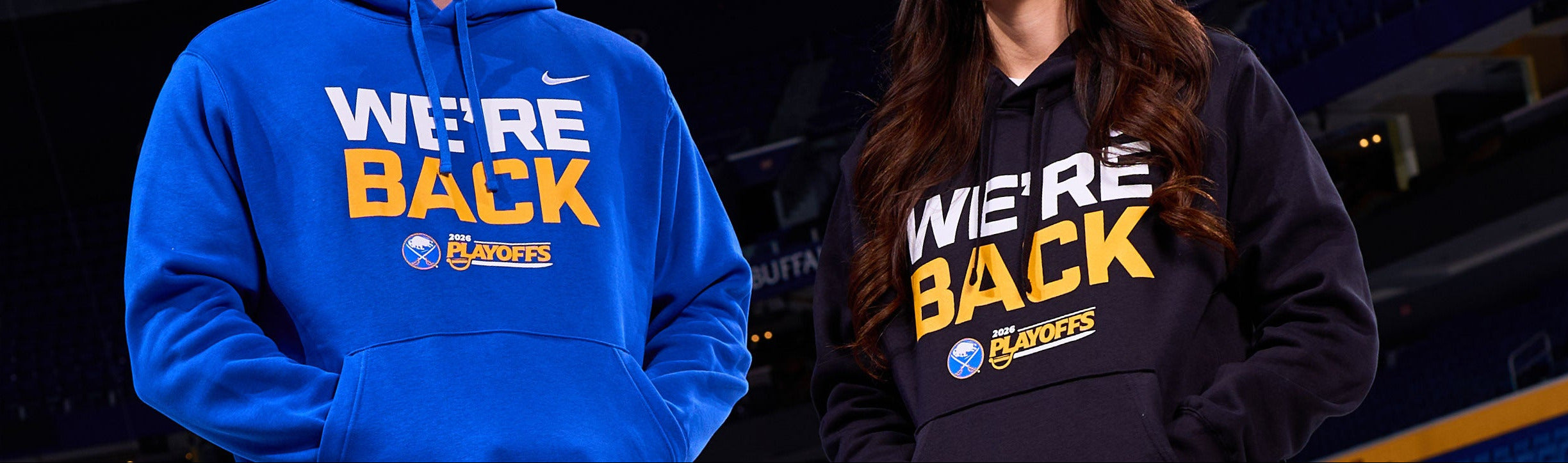 Two people wearing 'We're Back' hoodies with a sports team logo in the background.